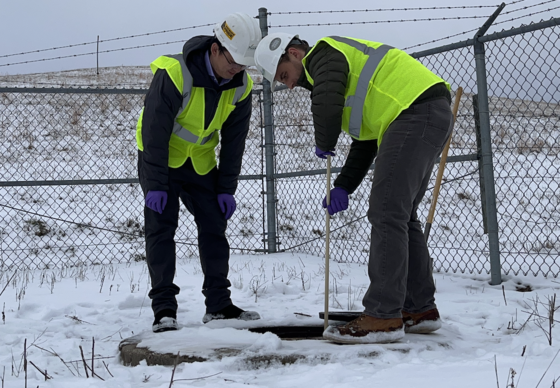 Two people in a snowy landscape drop a measuring device into a sewer to test for continents.